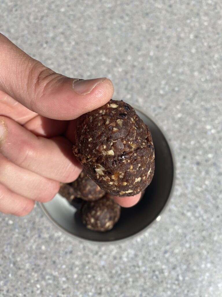 Close-up van een carob power balletje in de hand, met zichtbare stukjes havermout